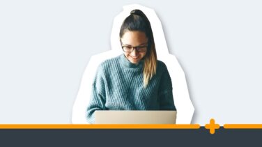 Młoda uśmiechnięta kobieta w okularach i swetrze pracująca przy laptopie