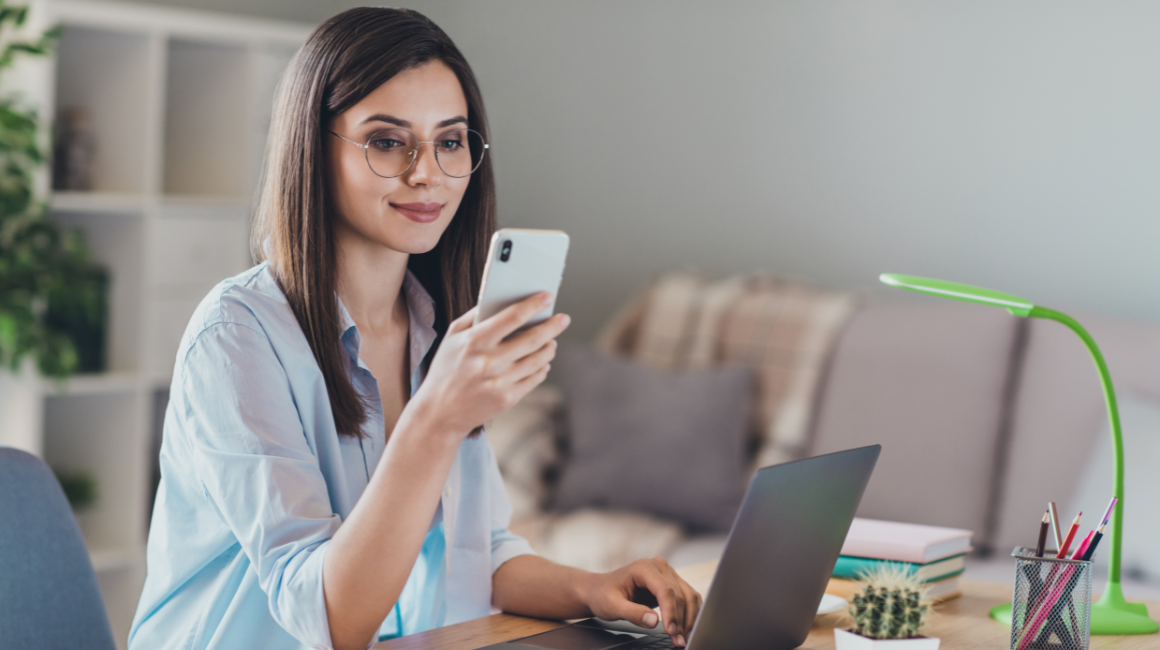 Kobieta w okularach sprawdza telefon przy laptopie